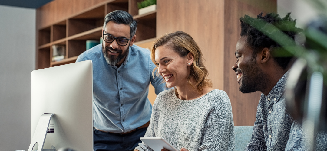 Three individuals collaborate around a computer in a modern office setting, focusing on a digital device.