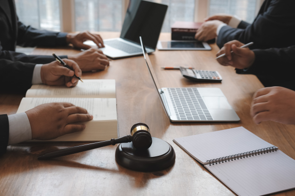 A meeting of professionals discussing legal matters, with a gavel, laptops, notepad, and books on a wooden table.