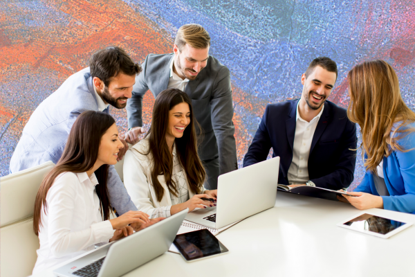 A diverse group of professionals collaborate over laptops and a tablet in a modern office, symbolizing teamwork and strategic planning for open enrollment success.
