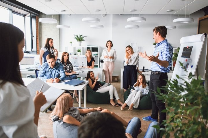 A diverse group of people engaged in a meeting, with one person presenting while others listen and take notes in a bright, modern office, discussing open enrollment