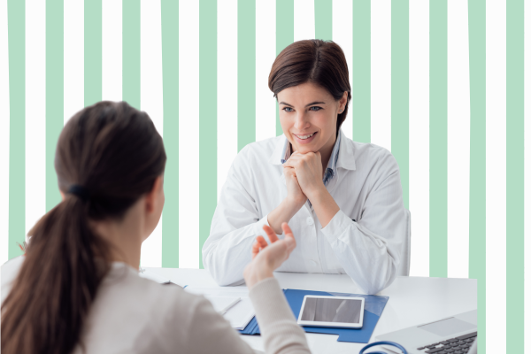 Two people engaged in a discussion at a desk with documents, a tablet, and a laptop, against a green and white striped background.